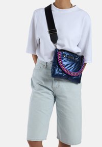 Sac matelassé marine avec une finition texturée, dot�é d'une bandoulière tissée colorée, d'accents métalliques et d'une fermeture à clip. À porter en bandoulière.