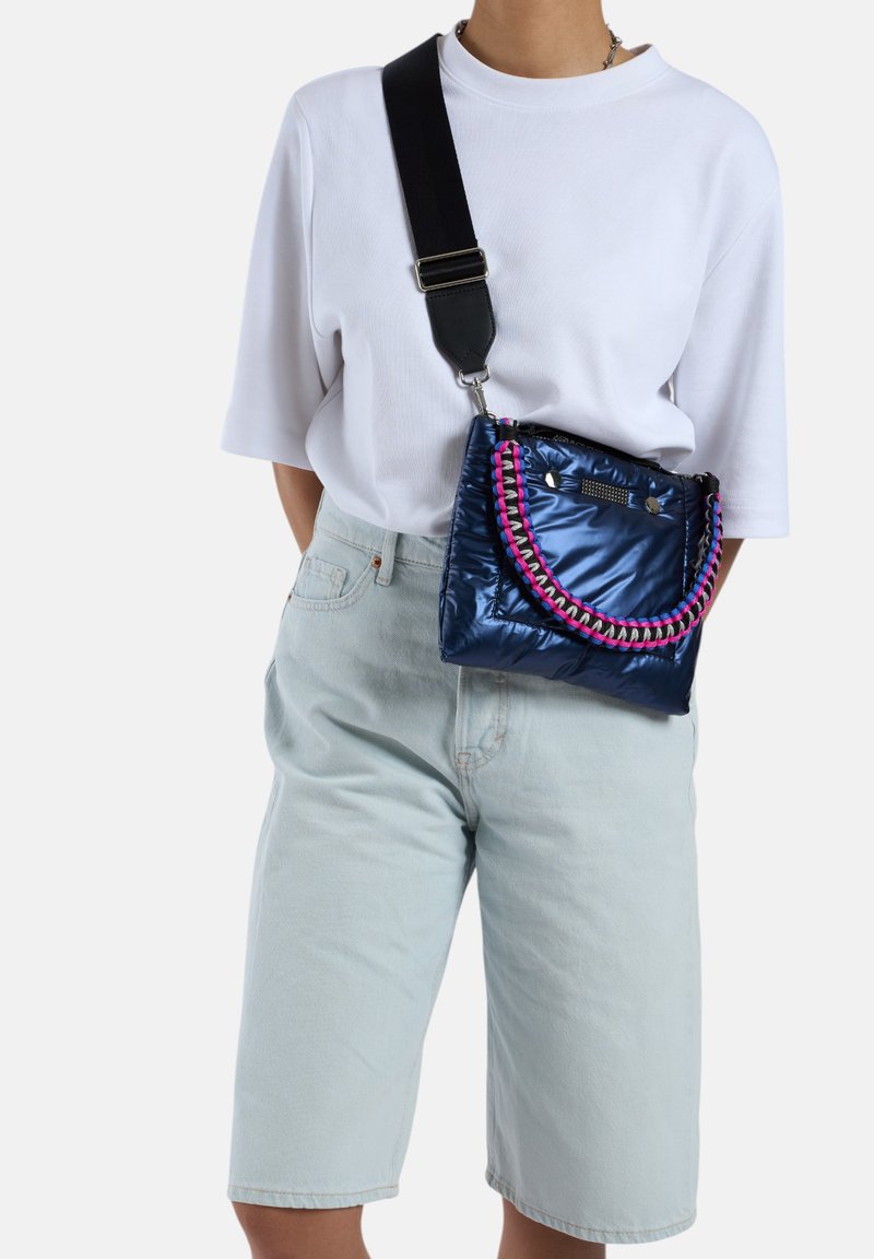 Sac matelassé marine avec une finition texturée, doté d'une bandoulière tissée colorée, d'accents métalliques et d'une fermeture à clip. À porter en bandoulière.