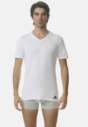 Valkoinen puuvillainen V-kaula-aukkoinen T-paita lyhyillä hihoilla, jossa on hienovarainen Adidas-logo vasemmalla puolella. Malli käyttää harmaita bokserishortseja.