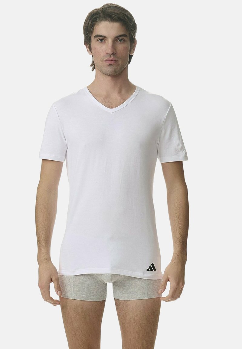 Vit bomulls-T-shirt med V-ringning och korta ärmar, med en subtil Adidas-logotyp på vänster sida. Modell iförd gråa kalsonger.