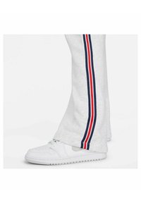 Graue Sweatpants mit geradem Schnitt und marineblauen sowie roten Seitenstreifen. Kombiniert mit weißen Sportschuhen auf einem neutralen Hintergrund.