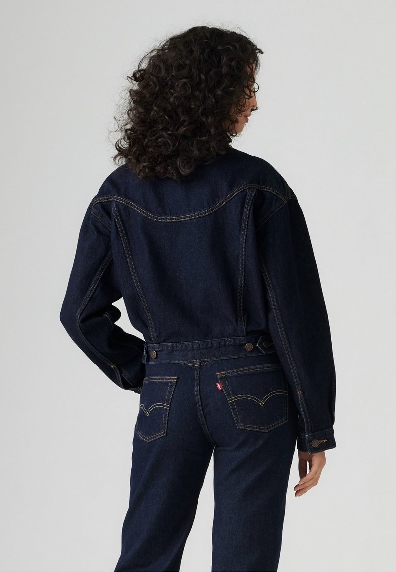 Giacca in denim blu scuro con una vestibilità rilassata, caratterizzata da un design con yoke, due tasche posteriori e cuciture a contrasto. Collo rotondo e dettagli con bottoni.