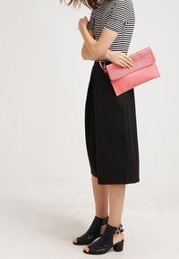 Mustat culottes-housut yhdistettynä raidalliseen t-paitaan, kädessä vaaleanpunainen perforoitu käsilaukku. Asun täydentävät mustat korolliset sandaalit.