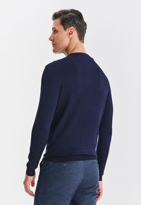 Granatowy sweter z długim rękawem wykonany z dzianiny o fakturze, z okrągłym dekoltem i prążkowanymi mankietami, widoczny od tyłu.