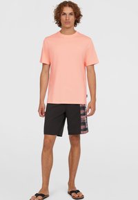 Lichtroze t-shirt met korte mouwen, gecombineerd met zwarte shorts met een kleurrijke, gedessineerde zijrand. Casual schoeisel maakt de look compleet.