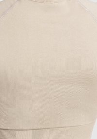 Beige sportieve crop top gemaakt van rekbare stof, met een ribbeltextuur en gladde naden. Eenvoudig ontwerp zonder zichtbare patronen of accenten.
