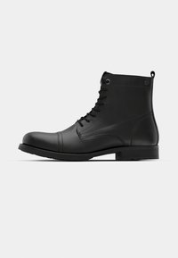 Botines de cuero negro hasta el tobillo con textura suave, punta redonda, cordones en la parte delantera y un tacón bajo en bloque. Presentan costuras reforzadas.