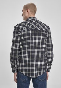 Marineblå og hvit rutete skjorte med lange ermer, spiss krage og buet kant, laget av teksturert stoff.