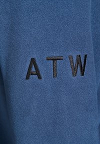 Niebieski polar o miękkiej fakturze, z haftowanymi czarnymi literami "ATW" z przodu.