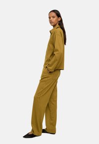 Musztardowy, w paski, dopasowany strój z długim rękawem i szerokimi spodniami; materiał wydaje się gładki i lekki.