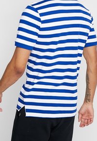 Blå och vitrandig kortärmad t-shirt, tillverkad av mjuk bomull, med rak fåll och sidospår för rörelsefrihet.