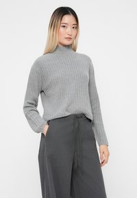Grå ribbestrikket turtleneck-genser med lange ermer, kombinert med antrasittgrå vide bukser med knyteliv. Glatt tekstur.