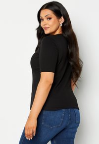 Maglietta nera a righe, a maniche corte, abbinata a jeans in denim blu aderenti; tessuto liscio con una silhouette leggermente aderente.