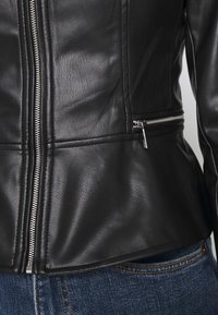 Giacca in pelle nera con texture liscia, caratterizzata da cerniere argentate e design aderente. Include tasche laterali con cerniera e dettaglio orlo curvo.