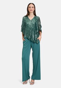 Top in paillettes teal con scollatura a V e maniche fluenti, abbinato a pantaloni a gamba larga coordinati. Sandali con tacco argentati completano il look.