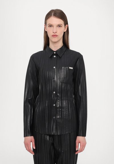 Chemise plissée noire en matériau brillant, dotée d'un col, d'une fermeture à boutons sur toute la longueur et d'une poche poitrine. La texture semble lisse avec des lignes verticales.