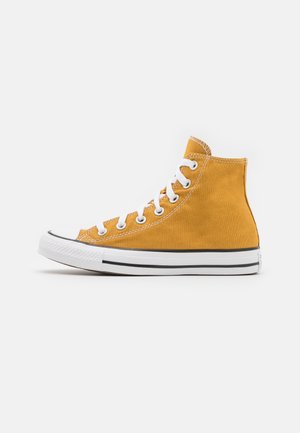 Gul kanvas høyhælte sneakers med hvite øyer og snører. Svarte gummisåler med hvite striper. Rund tåhette.