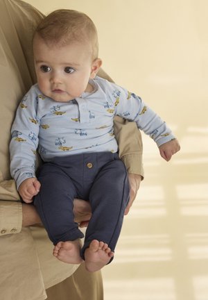 Camisa de manga larga azul claro con estampados de animales, combinada con pantalones azul marino con un botón. Bebé sostenido en los brazos de una persona.