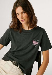 T-shirt nera a maniche corte e colletto rotondo; presenta una stampa grafica rosa e testo sul petto; tessuto in cotone morbido e traspirante.