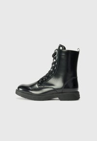 Stivaletto in pelle nera con finitura lucida, punta rotonda, lacci frontali e suola in gomma. Presenta un piccolo manico sul retro.