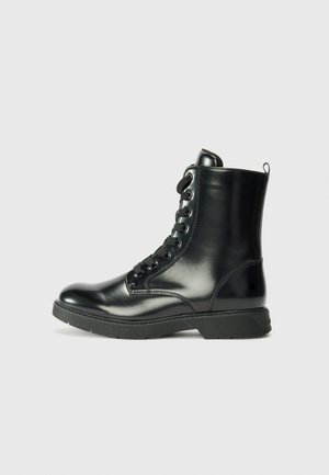 Bottine en cuir noir avec une finition brillante, bout rond, lacets à l'avant et semelle en caoutchouc. Elle possède une petite languette à l'arrière.