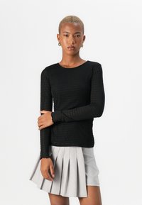 Top negro de manga larga con tejido texturizado y escote redondo, combinado con una falda plisada gris. Diseño sencillo y ajustado.