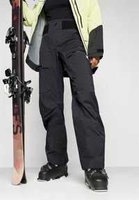 Schwarze Skihosen aus einem strapazierfähigen, wetterfesten Material. Mit Cargo-Taschen, einem Reißverschluss-Detail und einem verstellbaren Bund.