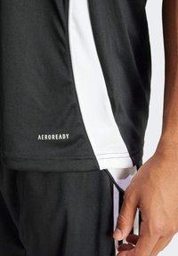 Camiseta deportiva negra con acentos blancos en los costados, hecha de tela ligera. Logotipo "AEROREADY" visible cerca del dobladillo. Textura y ajuste suaves.