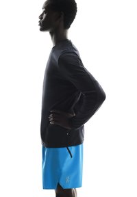 Sort langærmet atletisk top og lysblå shorts. Toppen har en rund halsudskæring og en smal pasform; shortsene har et logo og en snor i livet.