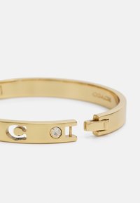 Gold metal cuff bracelet with a smooth finish, featuring a small clear crystal accent and cutout detailing on one side.