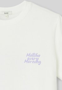 T-shirt en coton blanc avec un col rond et des manches courtes. Sur le devant, le texte « Matcha every Morning » est écrit en police cursive légère violet.