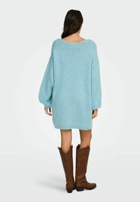 Gaiši zila, oversize stila adīta kleita ar garām piedurknēm un plašu izgriezumu, valkāta ar brūnām kovboju zābakām ar izšūtu detaļām.