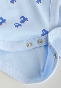 Hellblauer Baumwollbody mit einem wiederholten Muster kleiner blauer Lastwagen mit roten Rädern, ausgestattet mit Druckknöpfen am Schritt für einfaches An- und Ausziehen.