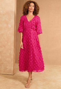 Rochie midi fucsia cu mâneci 3/4, dintr-un material texturat cu modele de puncte ridicate, decolteu în formă de v și fustă cu straturi. Purtați-o cu sandale cu barete.