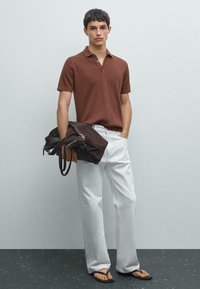 Brun texturerad polo skjorta med korta ärmar, vita raka byxor och svarta flip-flop sandaler. Bär en mörkbrun mockaväska.