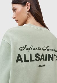 Felpa verde chiaro oversize con testo nero "Infinite Summer ALLSAINTS LONDON" sul retro. Tessuto morbido e vestibilità rilassata, collo a costine.