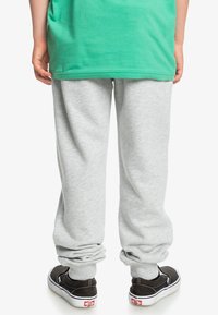 Pantalones de chándal grises con un ajuste entallado, puños elásticos y una textura suave, combinados con zapatos negros de tipo slip-on con acentos blancos.