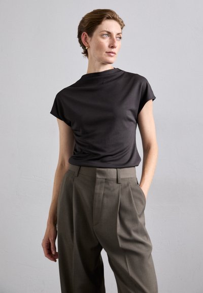 Black short-sleeve top with a high neckline, paired with high-waisted olive green trousers featuring pleats and a tailored fit.