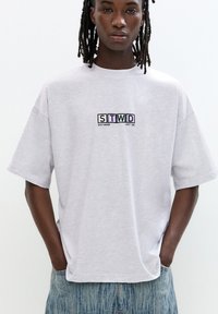 Light grey oversized T-shirt made of soft fabric with short sleeves. Embroidered logo "STWD" on the chest in various colors. Casual fit.