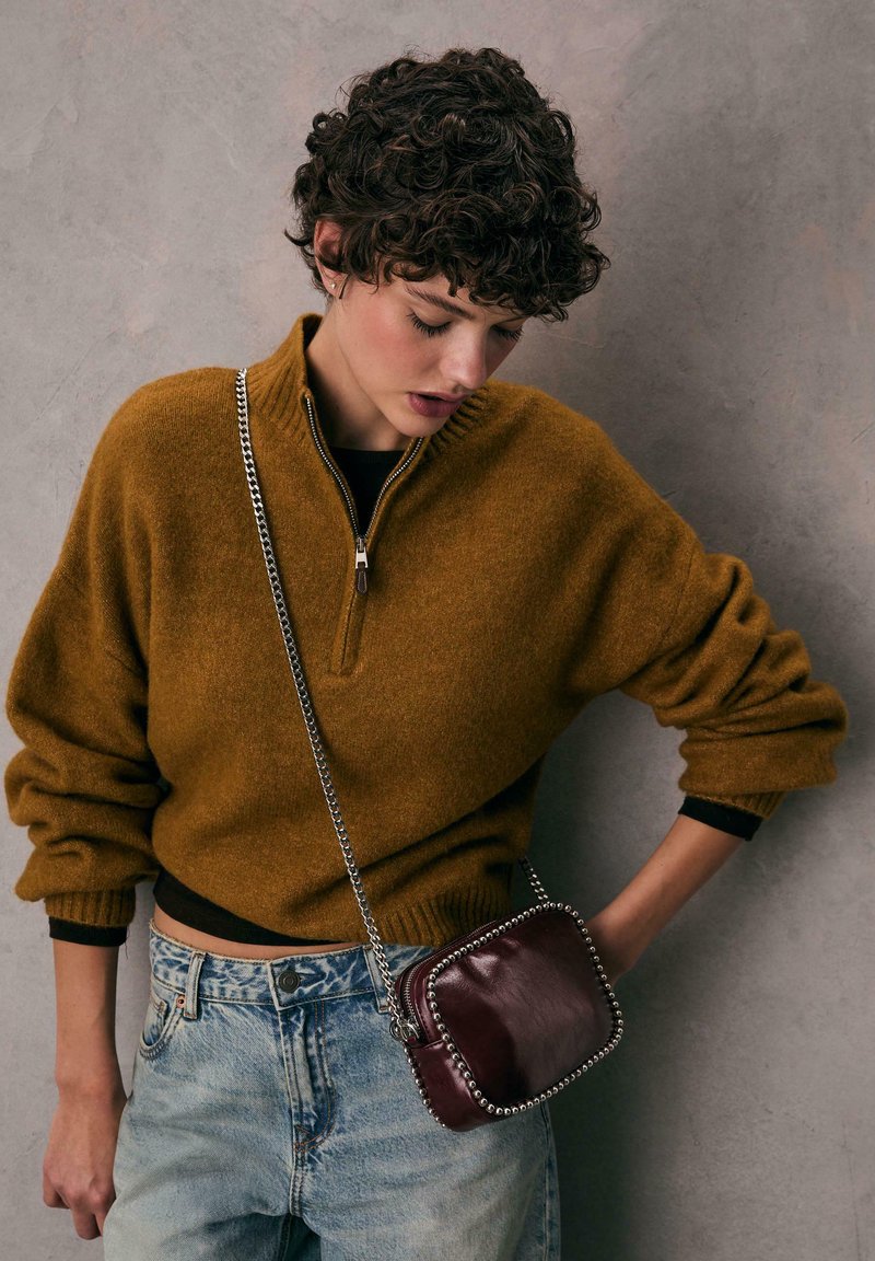 Brun zip-up sweater med ribbede manchetter, parret med lyseblå højtaljede jeans. Lille burgunder crossbody taske med sølvstuder og kædestrop.
