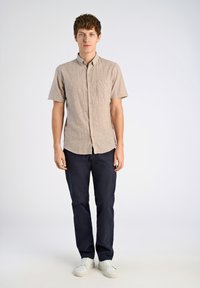 Ljusbrun, kortärmad, skjorta med krage och vertikala ränder, matchad med marinblå byxor och vita sneakers. Slim fit, detalj med framlomma.