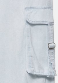 Tissu en denim bleu clair avec une grande poche rectangulaire dotée d'un rabat et d'une boucle rectangulaire en argent sur le côté droit.