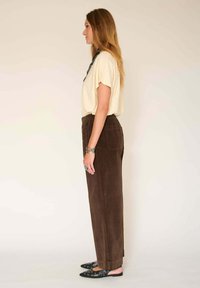 T-shirt beige à manches courtes, pantalon en velours côtelé marron et ballerines noires avec des embellissements, présentées de côté sur un fond uni.