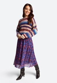 Daugiaspalvė megzta palaidinė su raudonomis, mėlynomis ir kreminėmis juostomis. Plazdanti purpurinė gėlių sijonas ir juodos kulkšnies auliniai batai ant kulno.