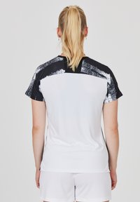 Kortærmet atletisk skjorte med en hvid krop og sorte samt teksturerede penselstrække accenter på skuldrene og ryggen. Glat stof.