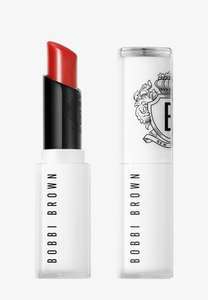 Rød leppestift i hvit tube med svart tekst "BOBBI BROWN"; matchende lukket hette med våpenskjoldlogo ved siden av på hvit bakgrunn.
