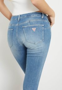 Ljusblå denimjeans med en figursydd design, med en triangel-logotyp på bakfickan och subtila blekningsdetaljer.