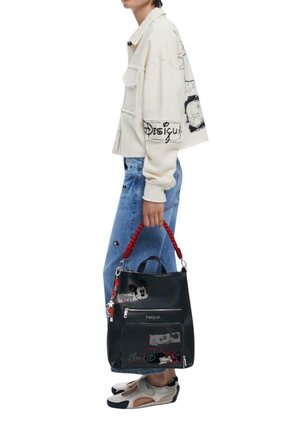 Black faux leather bag with red handle, featuring Mickey Mouse graphics and zippers, paired with a cream oversized jacket and blue jeans.