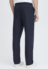 Navy blue trousers made of soft fabric with an elastic waistband, straight leg design, and two back pockets with button accents.
