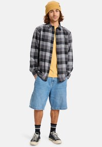 Black and gray checkered flannel shirt, yellow t-shirt underneath, light blue denim shorts, black sneakers, and yellow knit beanie.
